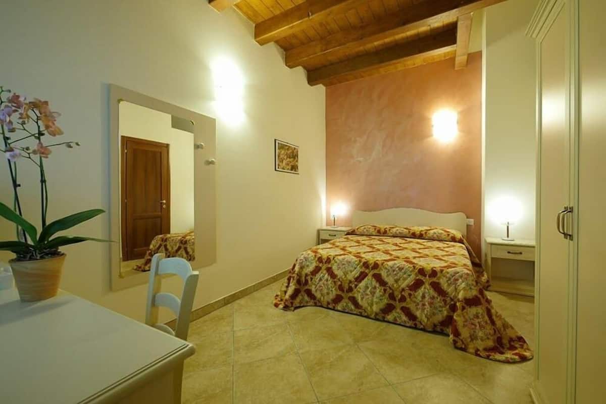 A bedroom with a bed, a chair, a desk, and a potted plant.