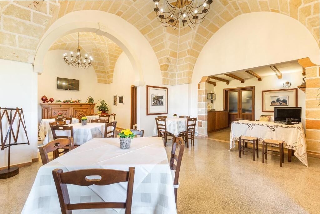 A dining area with tables and chairs, a chandelier, and a stone wall.