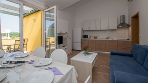 A modern kitchen with white cabinets, a microwave, and a sink. There is a dining area with a table set for a meal, and a blue sofa in the living area. - Villas Faro (Umag)