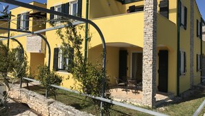A yellow building with stone pillars, a patio with outdoor furniture, and a stone wall. - Villas Faro (Umag)