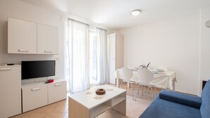 A modern living room with a flat-screen TV, a dining area with a table and chairs, and a blue sofa. - Villas Faro (Umag)