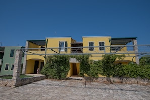 Un bâtiment à deux étages, doté d’une façade jaune, de piliers en pierre et d’une cour pavée de pierres.