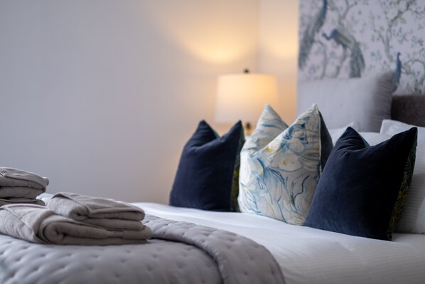 A neatly made bed with folded towels, dark blue and patterned pillows, and a wall with a tree design. - Ynys Arms (Swansea)