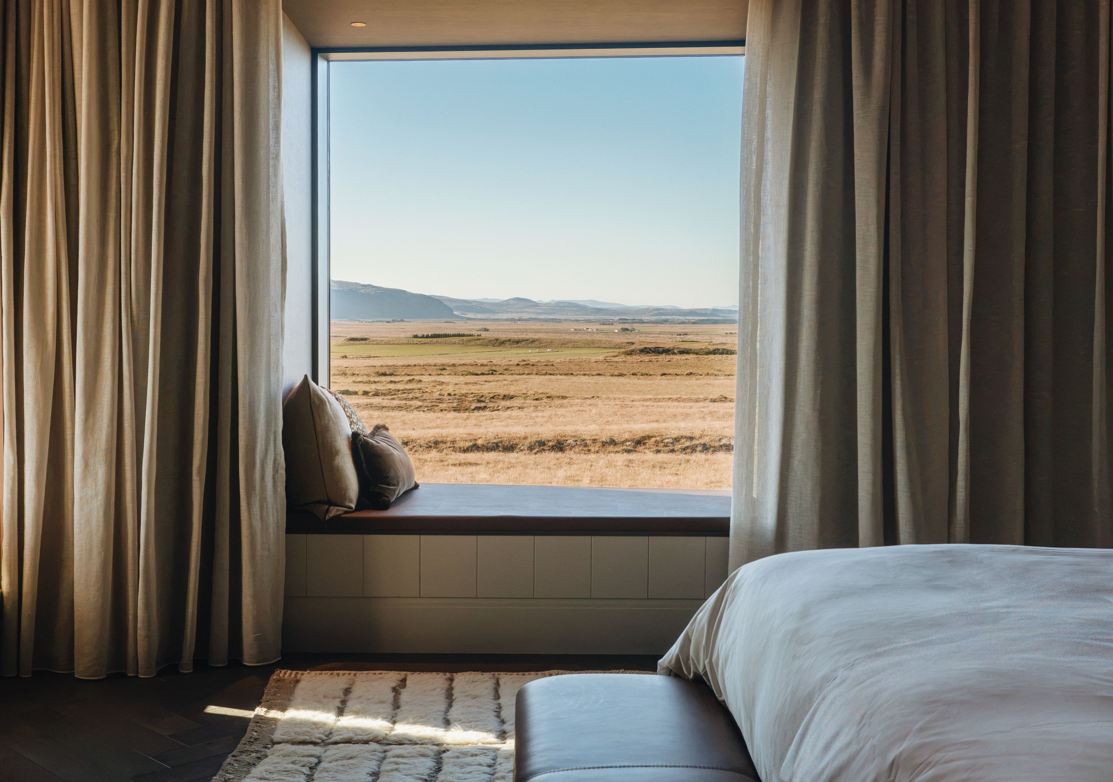 A bedroom with a large window, a bed, and a view of a landscape.