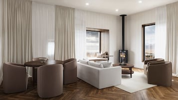 A modern living room with a sofa, chairs, a table, a fireplace, and large windows.
