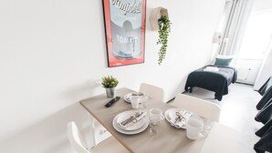 Et pænt spiseområde med et bord dækket til to, en hængende plante og et billede i ramme på væggen.
