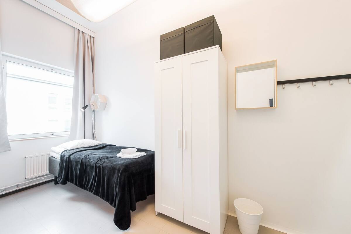 A bedroom with a bed, a wardrobe, a radiator, a window with curtains, a mirror, and a wall-mounted towel rack.