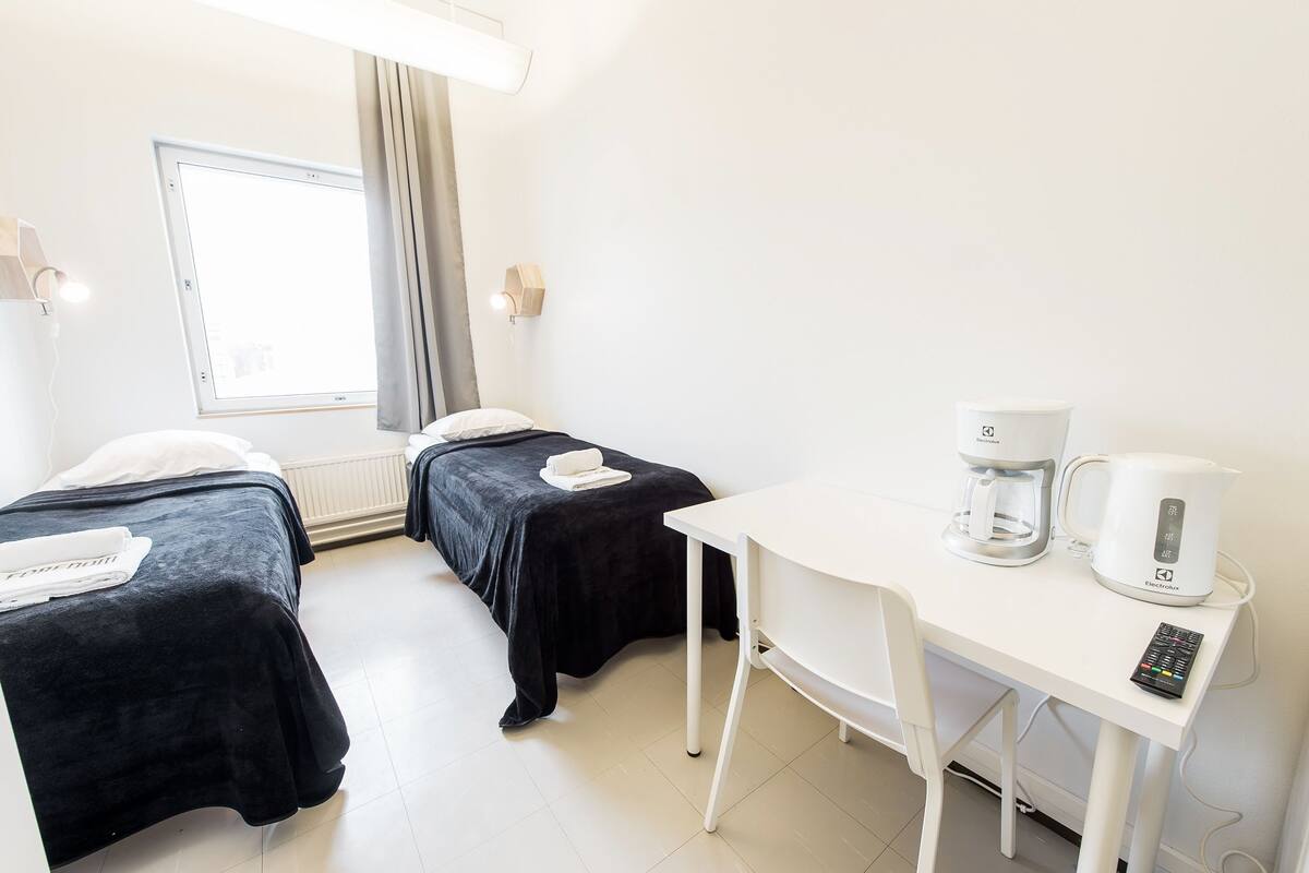 A hotel room with two beds, a white desk, a coffee maker, and a remote control.
