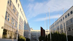 En moderne bygning med en central indgang, store vinduer og en parkeringsplads.