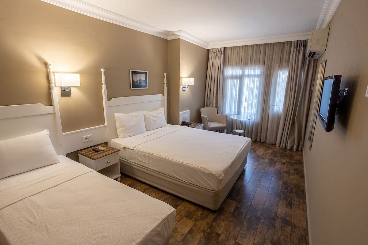 A hotel room with two beds, a desk, a chair, a TV, and a window with curtains.