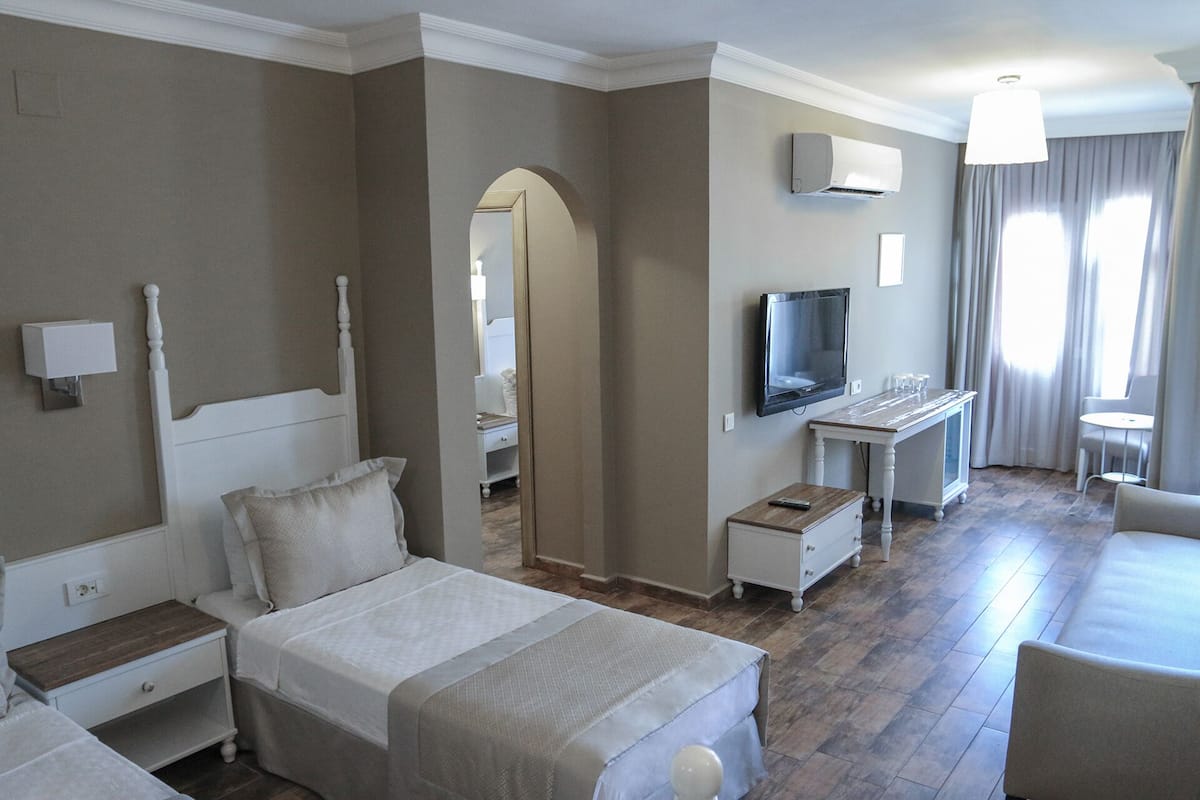A hotel room with a bed, bedside table, TV, desk, chair, and a window with curtains.