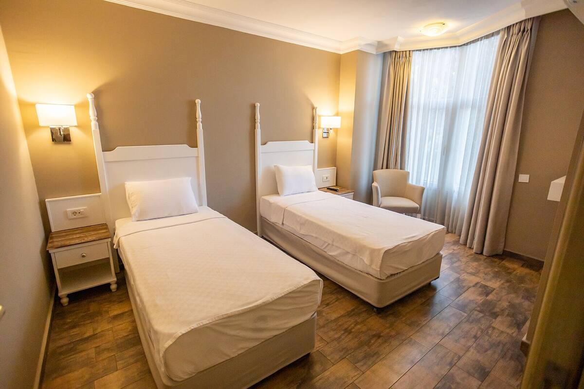 A hotel room with two single beds, a chair, and a nightstand with a lamp.