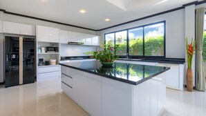 A modern kitchen with white cabinets, a black countertop, and a large window. - Grand Villa Luxury Holidays Phuket (Choeng Thale)