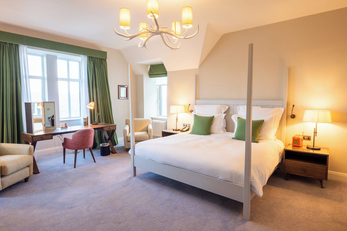 A bedroom with a four-poster bed, a desk, a chair, and a nightstand with a lamp.