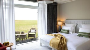 Une chambre d’hôtel avec un lit, une table de chevet, une lampe, une chaise, une petite table et une vue sur l’extérieur.