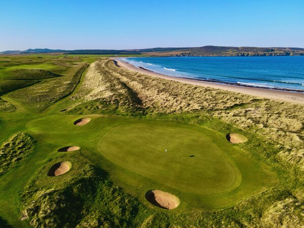 A golf course with bunkers, a beach, and a view of the ocean. - Another Place, The Machrie (Islay Island)