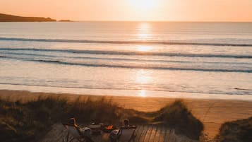 A wooden deck with chairs and a fire pit overlooking the ocean at sunset.