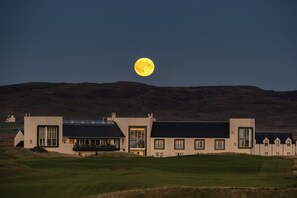 A building with a flat roof and large windows, set against a backdrop of hills and a full moon. - Another Place, The Machrie (Islay Island)