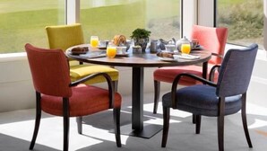 Un coin repas avec une table dressée pour quatre personnes et de grandes fenêtres donnant sur un paysage verdoyant.