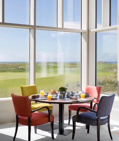 A dining area with a table set for four, large windows offering a view of a green landscape.