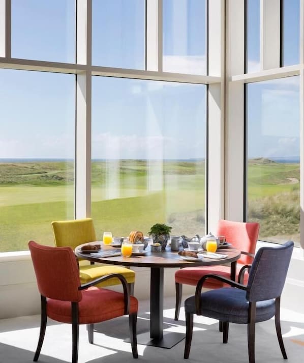 Un coin repas avec une table dressée pour quatre personnes et de grandes fenêtres donnant sur un paysage verdoyant.