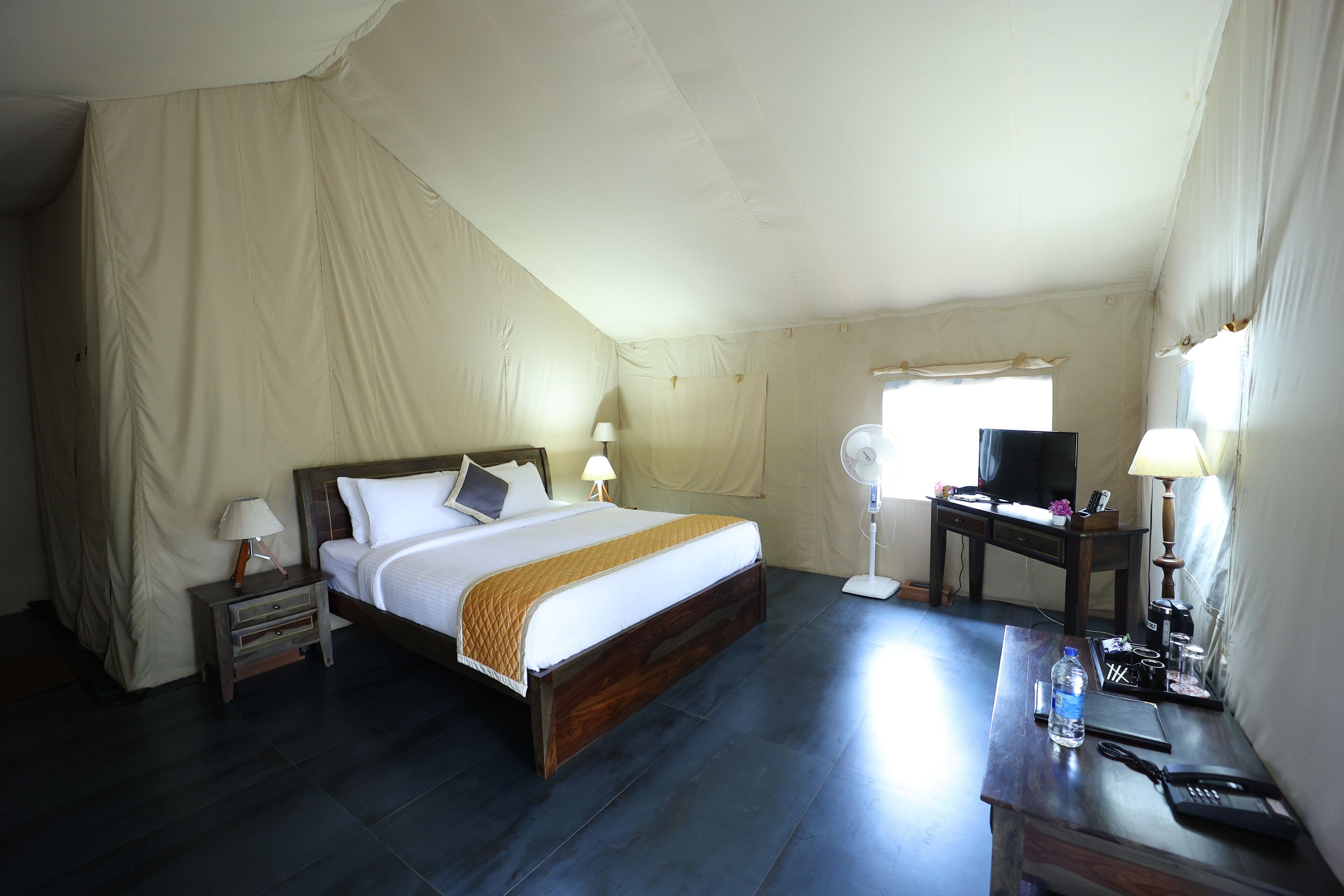 A bedroom with a bed, bedside tables, a desk, a chair, a television, and a window.