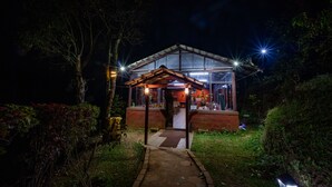 A well-lit, two-story building with a covered entrance and a visible dining area inside. - Three Hills Resort & Spa, Coorg (Madikeri)