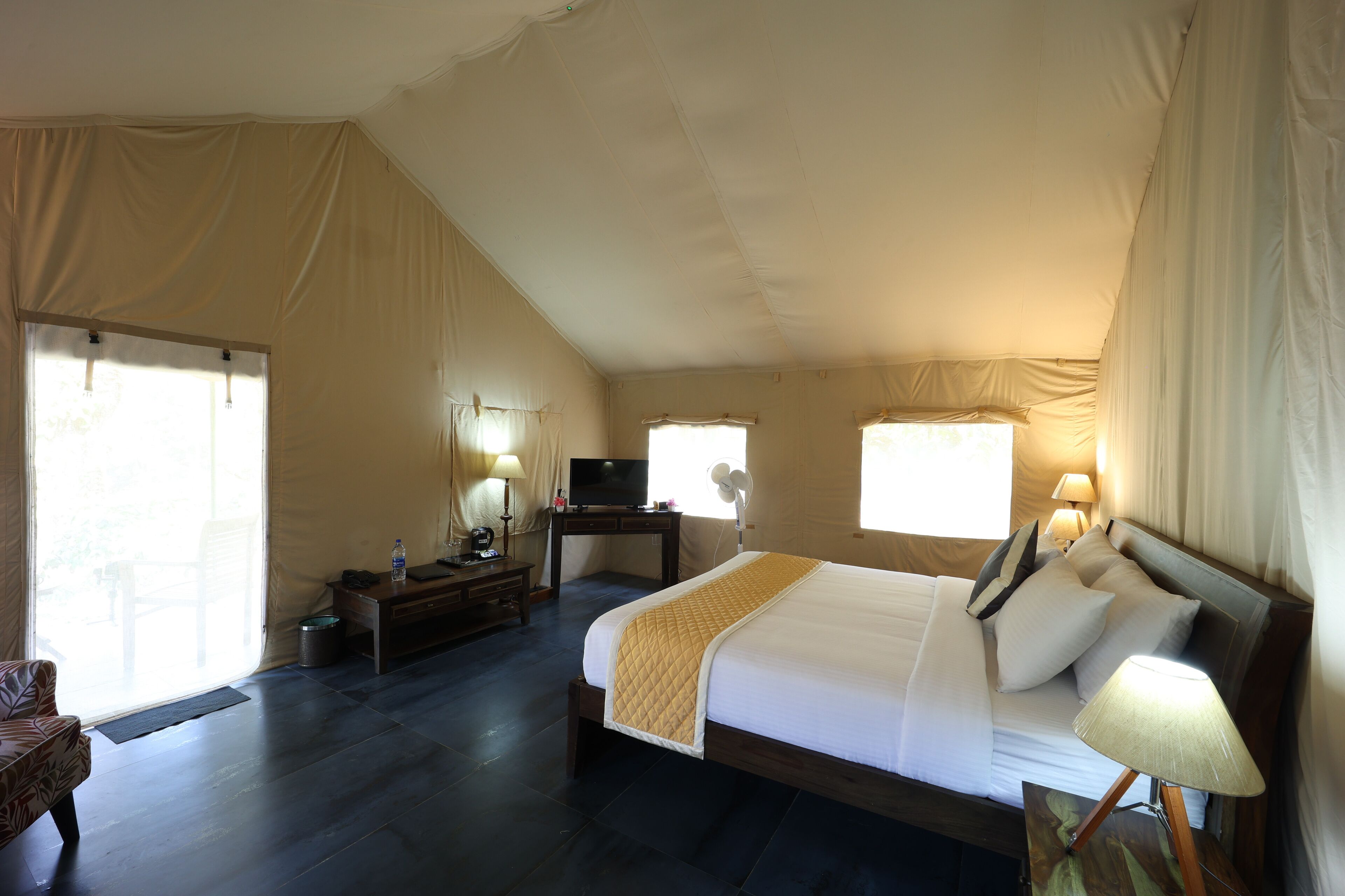 A spacious tent-style room with a large bed, two bedside tables with lamps, a television, and a desk with a chair.