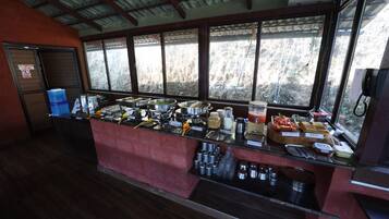 Un mostrador de buffet con diversas opciones de comida y bebidas, un teléfono y una ventana con vistas a árboles.