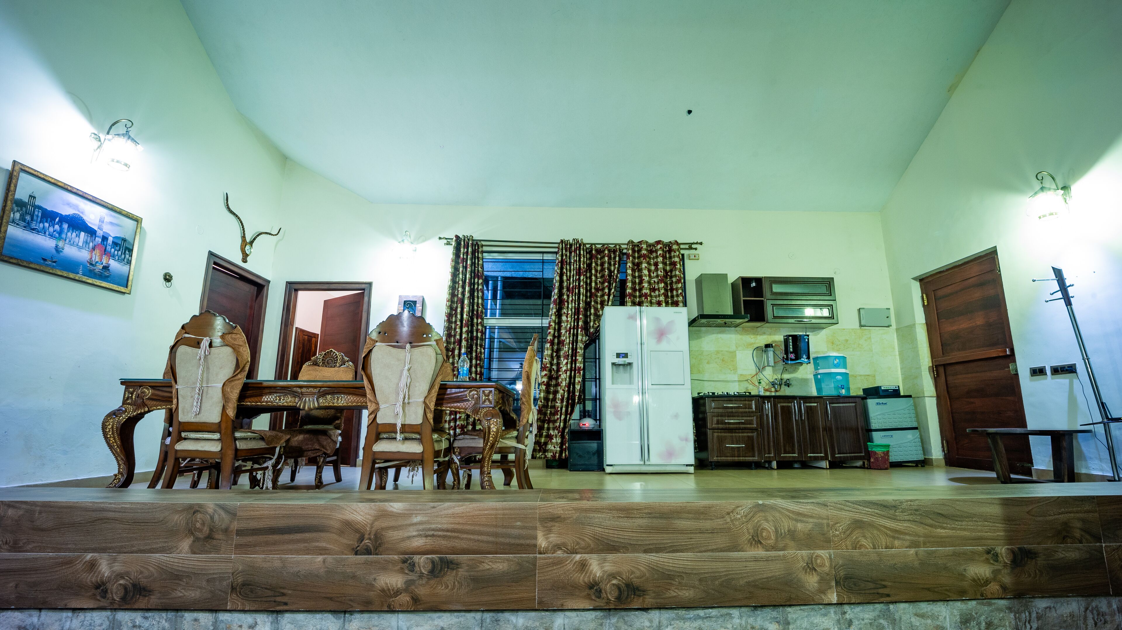 A dining area with a wooden table and chairs, a refrigerator, and a kitchen area with cabinets and a microwave.