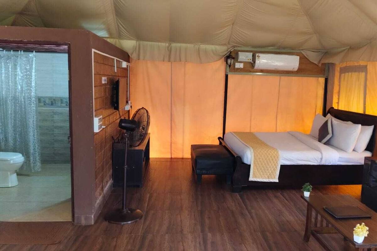Una habitación con tienda de campaña, una cama, un sofá, una mesita, un ventilador y una ventana con cortinas.