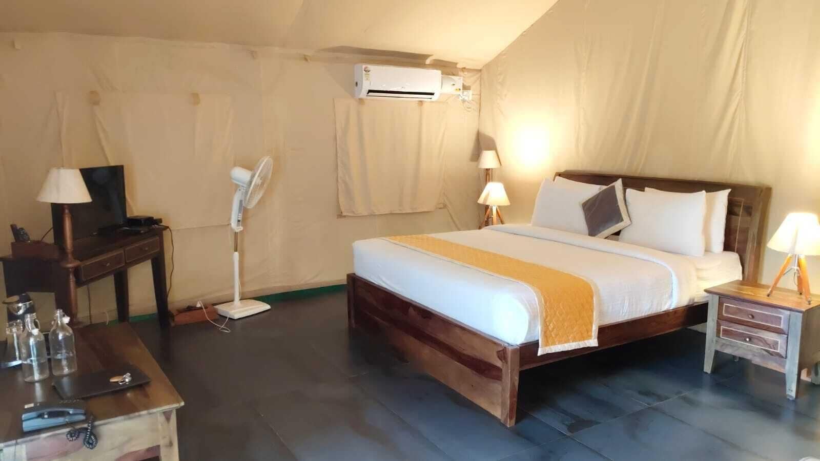 Un dormitorio con cama, mesitas de noche, escritorio, lámpara, aire acondicionado y ventilador.