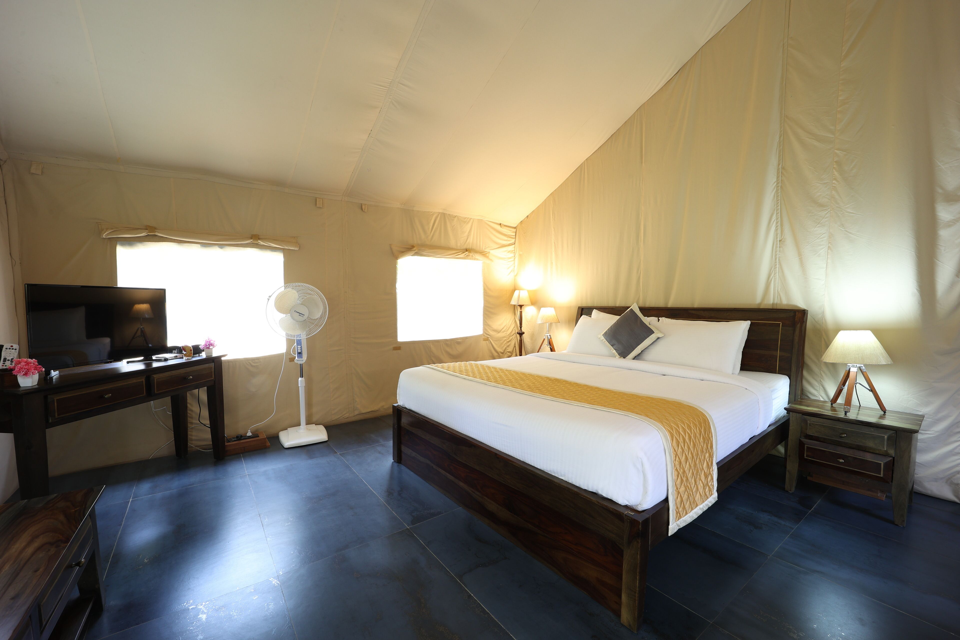 A bedroom with a bed, bedside tables, a desk, a TV, and a fan.