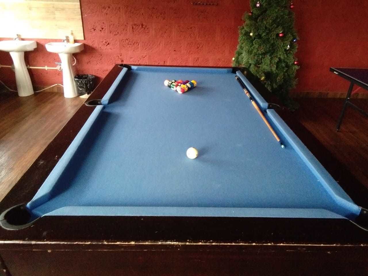 A pool table with balls, a Christmas tree, and two sinks in a room with a red wall.