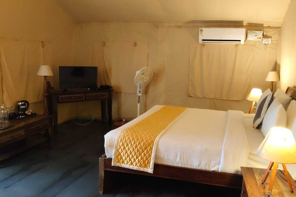 Habitación de hotel con cama, lámparas de noche, escritorio con televisor, ventilador y aire acondicionado.