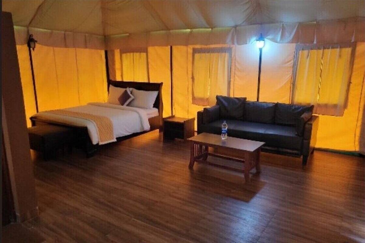 Una habitación tipo tienda de campaña con cama, sofá, una mesita y una botella de agua.