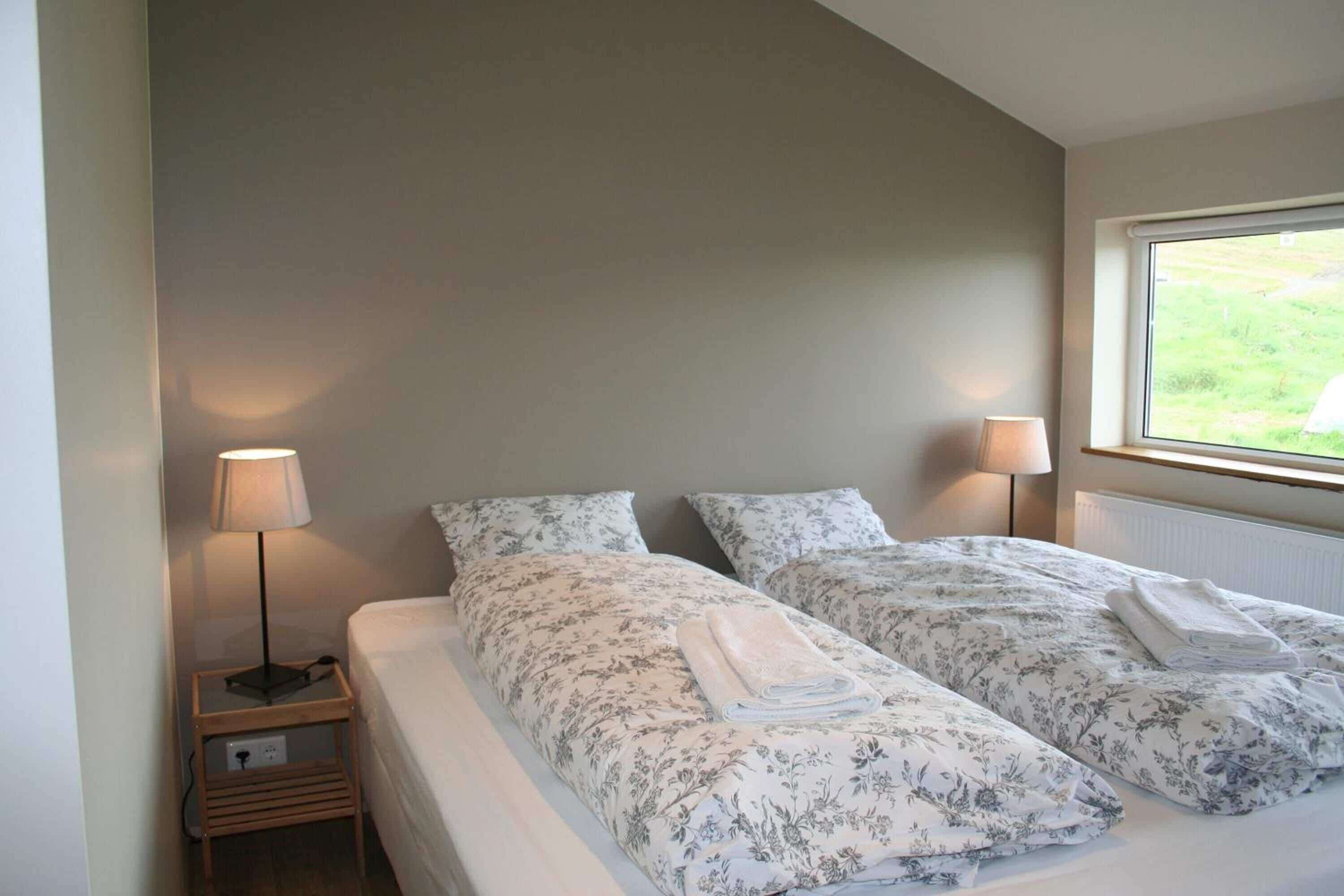 Hotelkamer met twee bedden, elk voorzien van bloemenprint beddengoed en handdoeken, een bedlampje en een raam met uitzicht op groen.