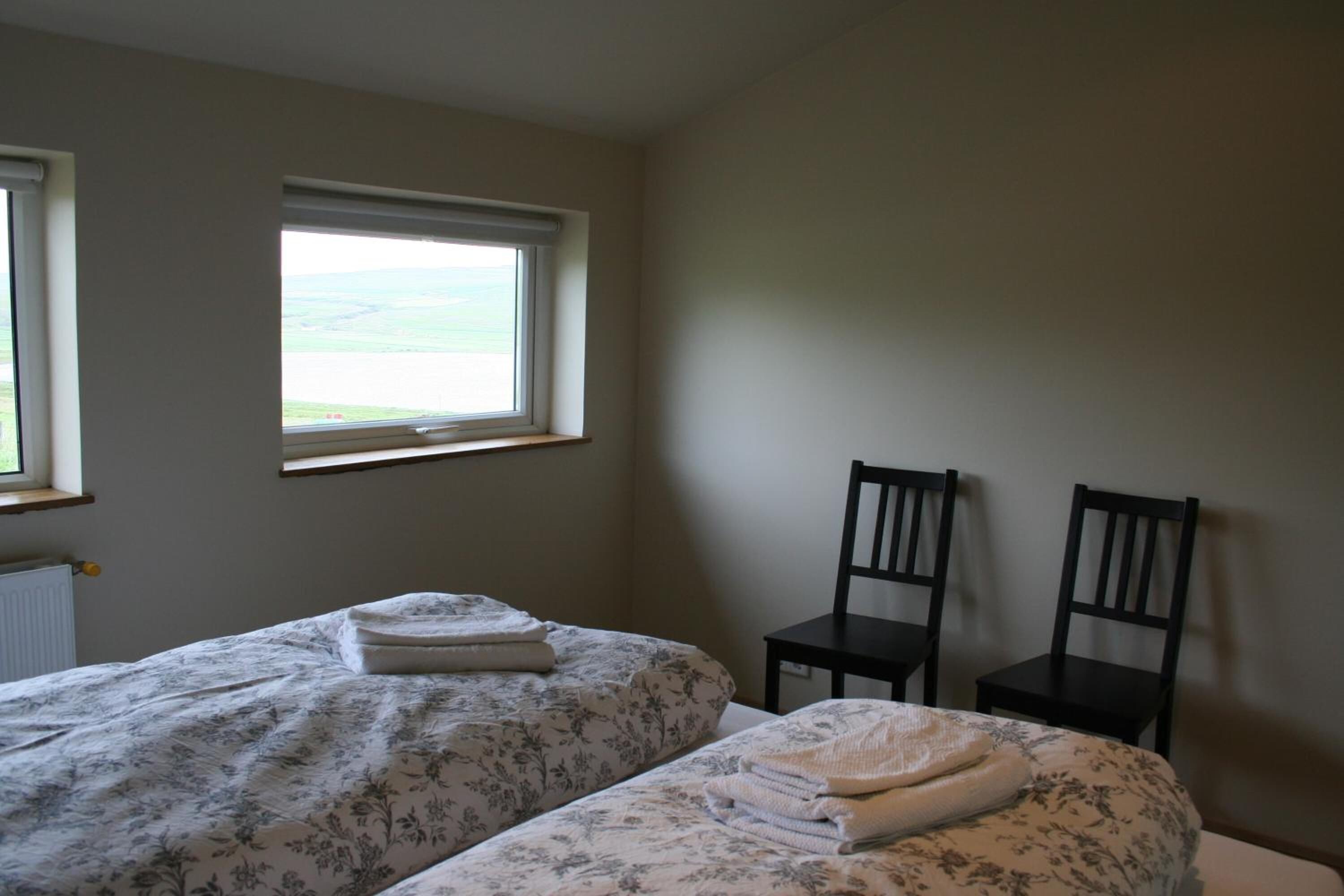 Une chambre avec deux lits, une fenêtre et deux chaises.