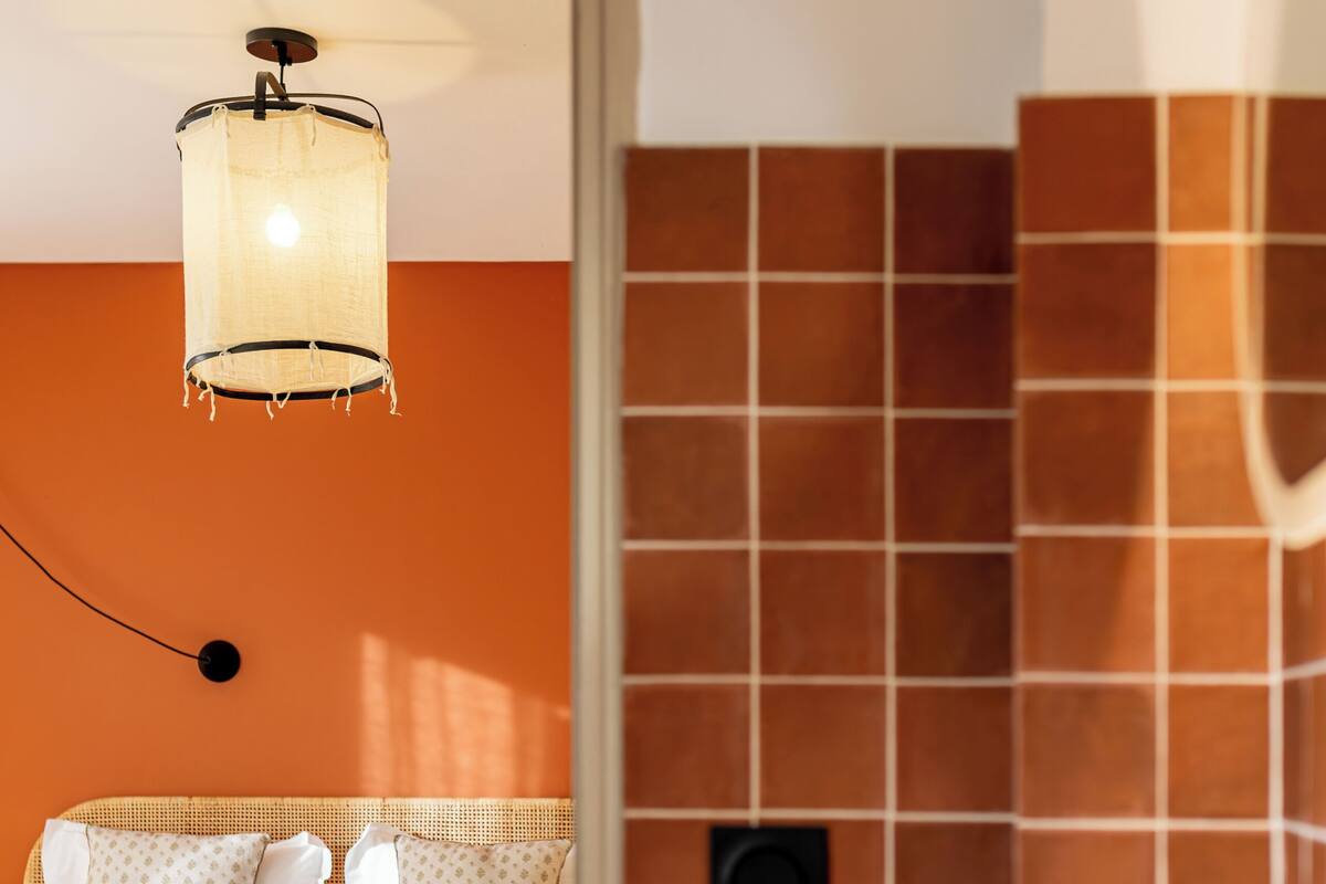 A hotel room with a bed, a bedside table, a lamp, and a tiled wall.