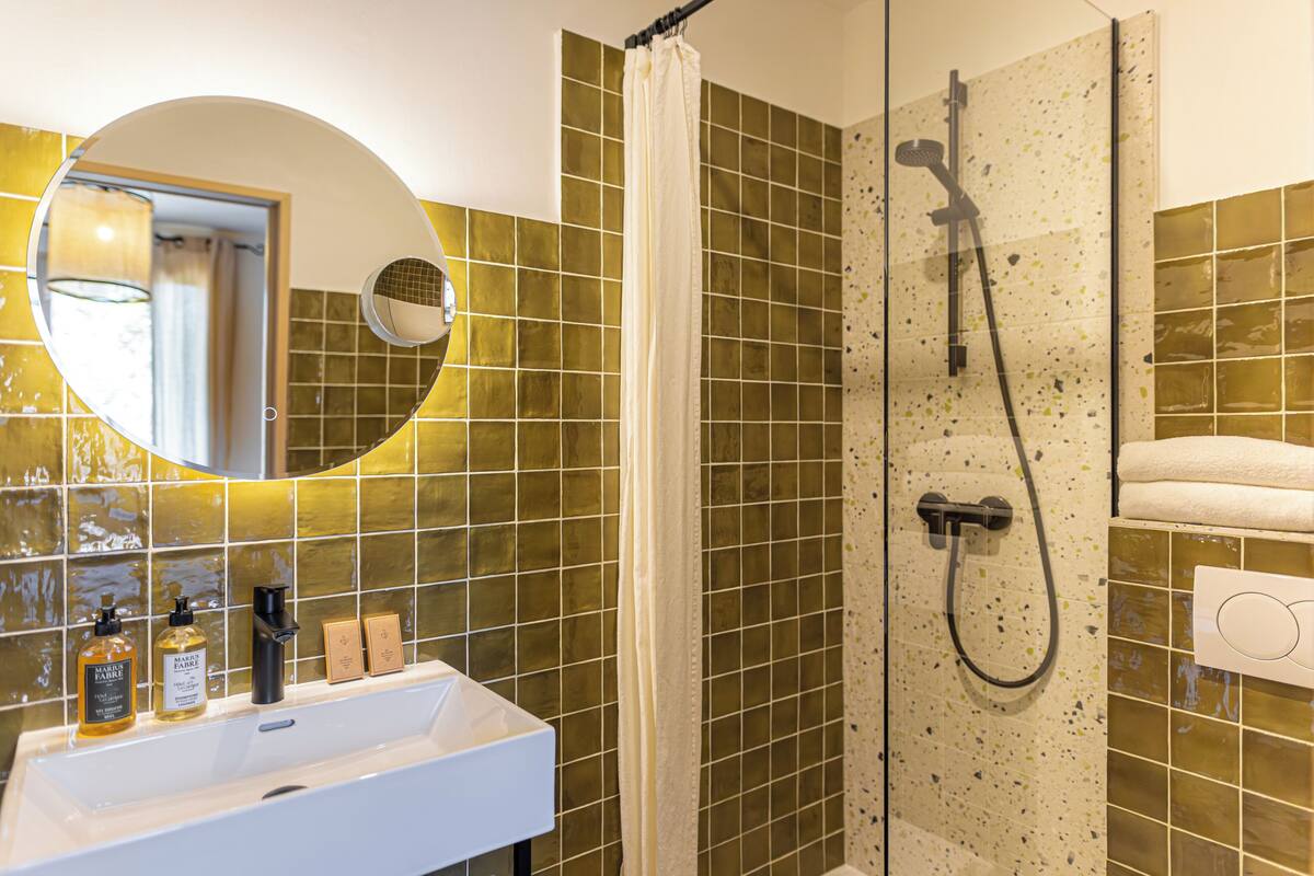 A bathroom with a shower, a sink with toiletries, and a mirror.