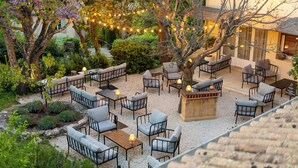 An outdoor seating area with multiple tables and chairs, surrounded by trees and plants.