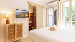 A hotel room with a bed, a television, a cabinet, and a window with a view of greenery. - La Garrigue (Venasque)