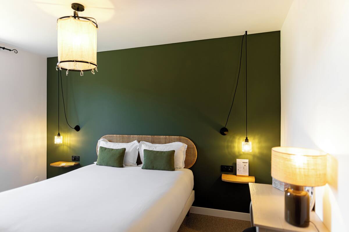 A hotel room with a bed, bedside lamps, a nightstand, and a wall-mounted lamp.
