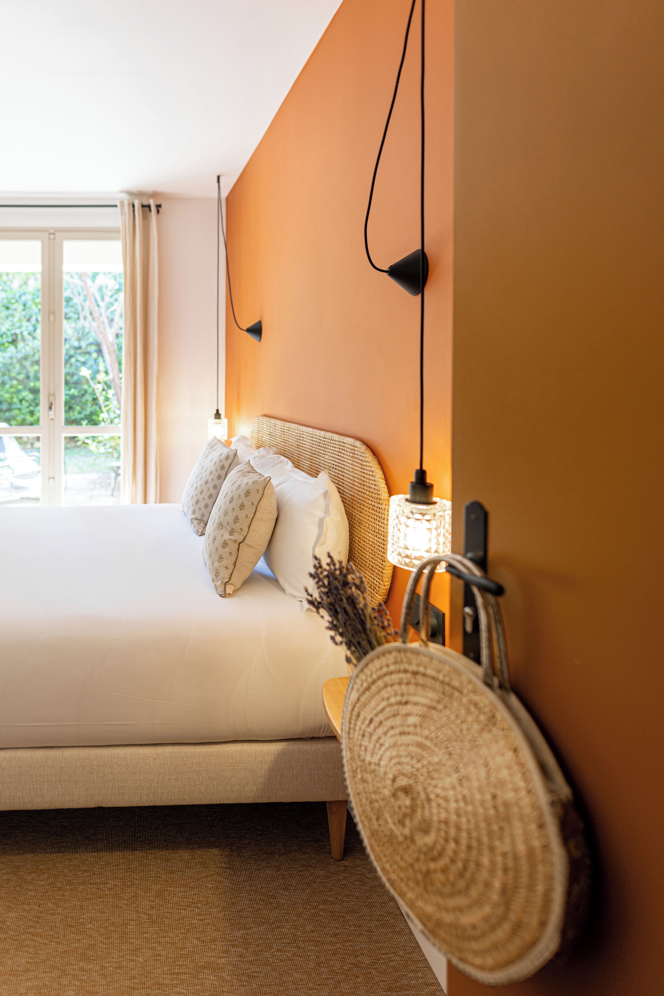 Ein Schlafzimmer mit einem Bett, einer Nachttischlampe und Blick ins Freie.