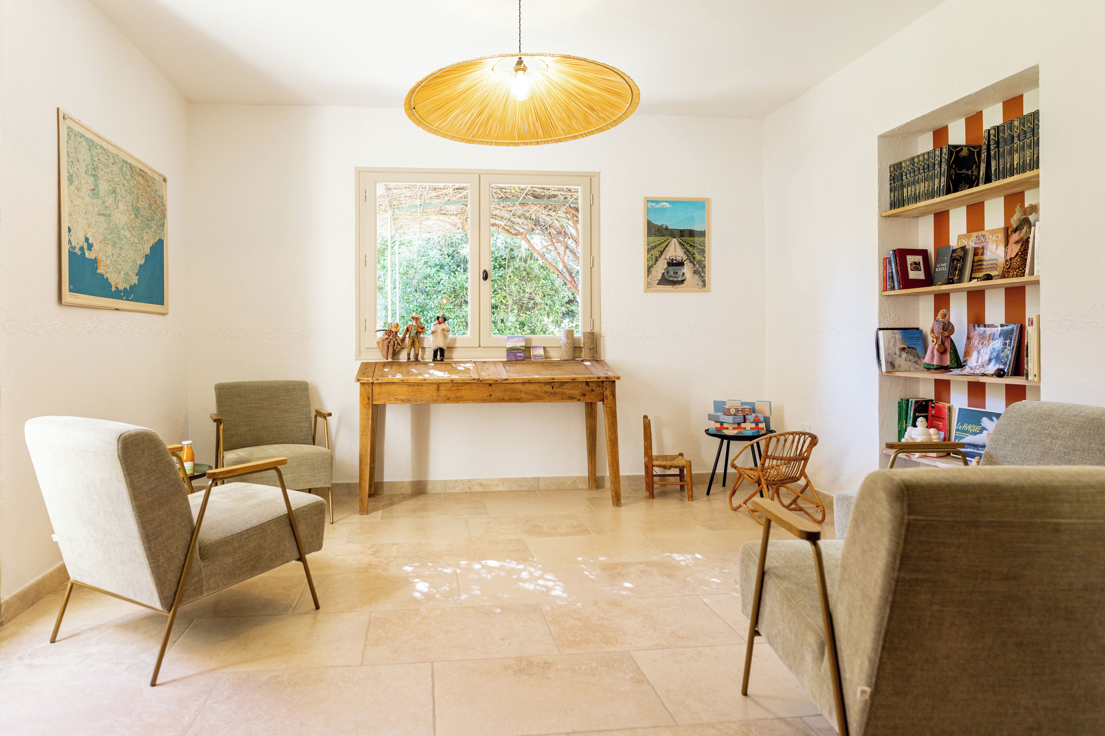 Una sala de estar con una mesa de madera, dos sillas, una estantería y un ventanal con vistas a árboles.