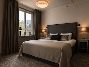A hotel room with a large bed, two bedside tables, a window with curtains, and a view of buildings outside. - Hotel Ranten (Falkoping)