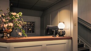 A reception area with a wooden counter, a vase of flowers, a coffee machine, and a staircase in the background. - Hotel Ranten (Falkoping)