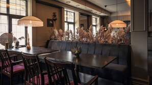 A restaurant interior with a long table, cushioned seating, pendant lighting, and decorative plants. - Hotel Ranten (Falkoping)