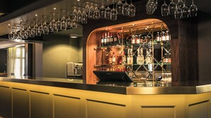 A bar area with a counter, shelves of bottles, and hanging wine glasses. - Hotel Ranten (Falkoping)