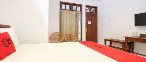 A hotel room with a bed, a desk, two wicker chairs, a TV, and a door with a window.